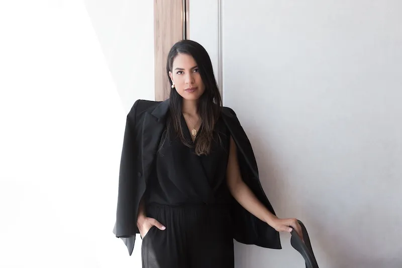 Isis Alpoim Scardua in a black outfit, standing beside a window