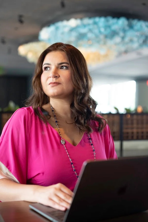 Jamile Moraes Pellicer in a pink blouse, working on a laptop